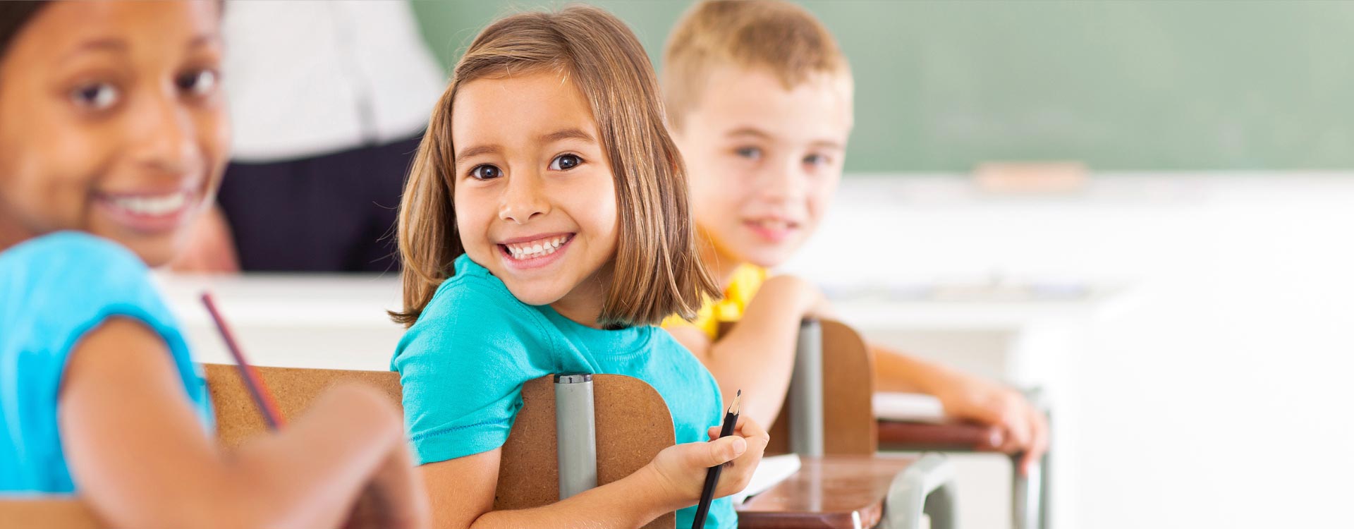 Children smiling while sitting at their school desk.